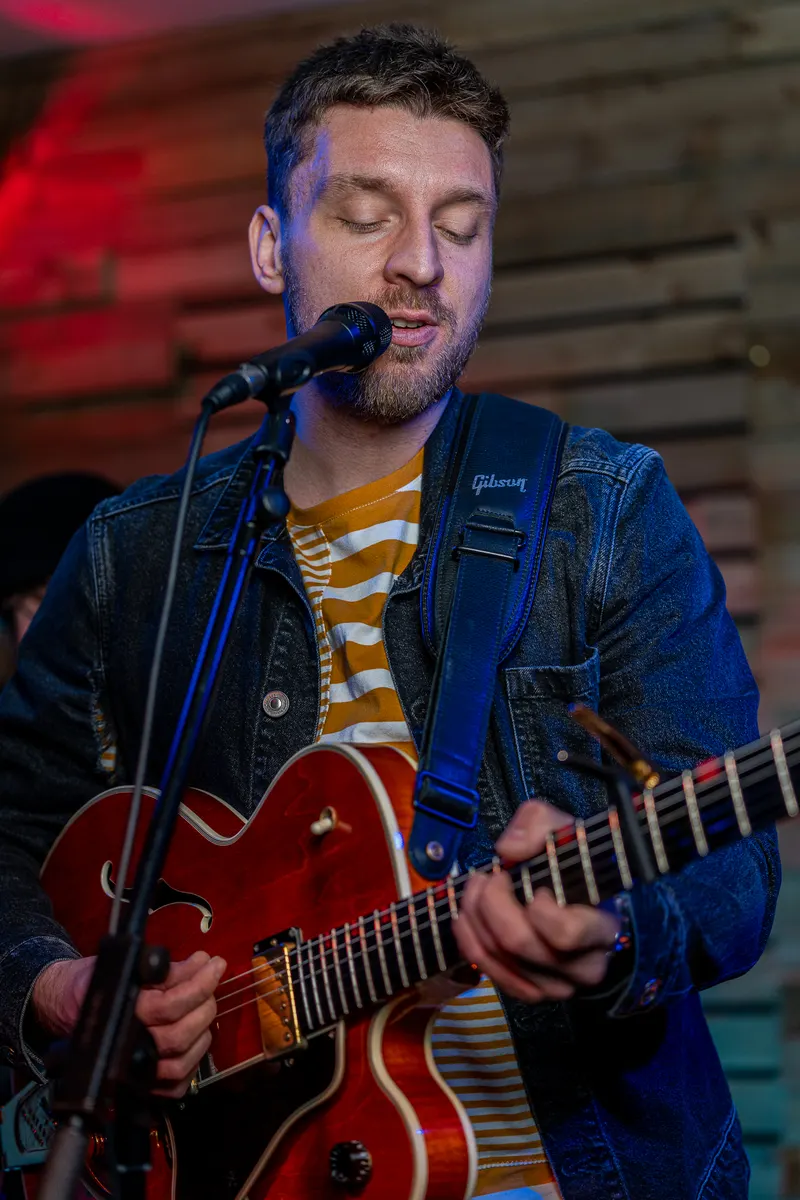 Tom Ryder performing with a red hollow-body guitar