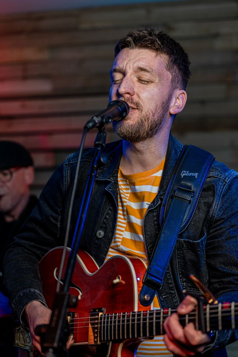 Tom singing and playing a red Gibson guitar, eyes closed