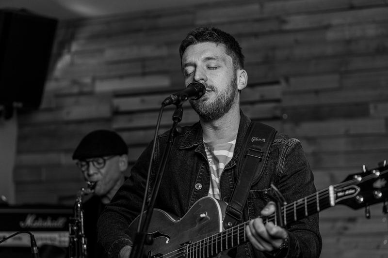 Black and white photo of Tom singing with his guitar