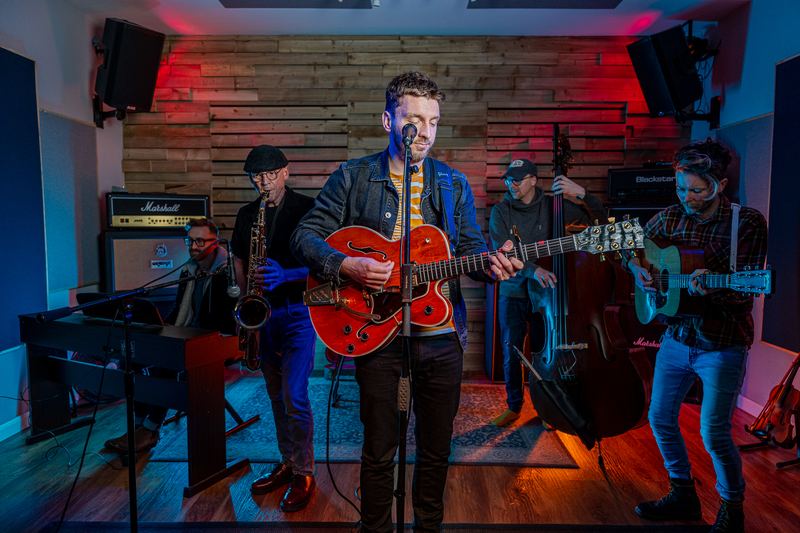 Tom and his band playing in a rehearsal room lit red and blue